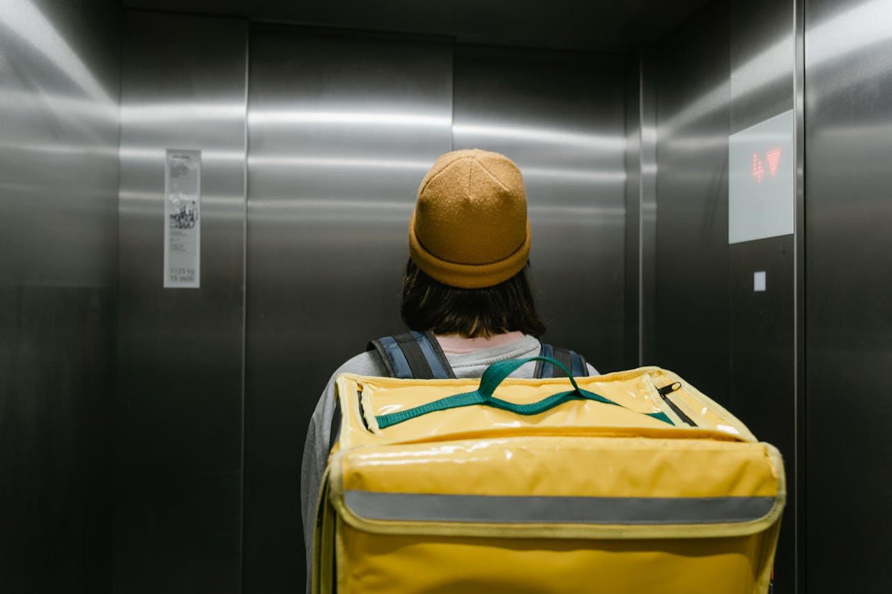 Courier in an elevator with a large yellow thermal backpack, ready for delivery.