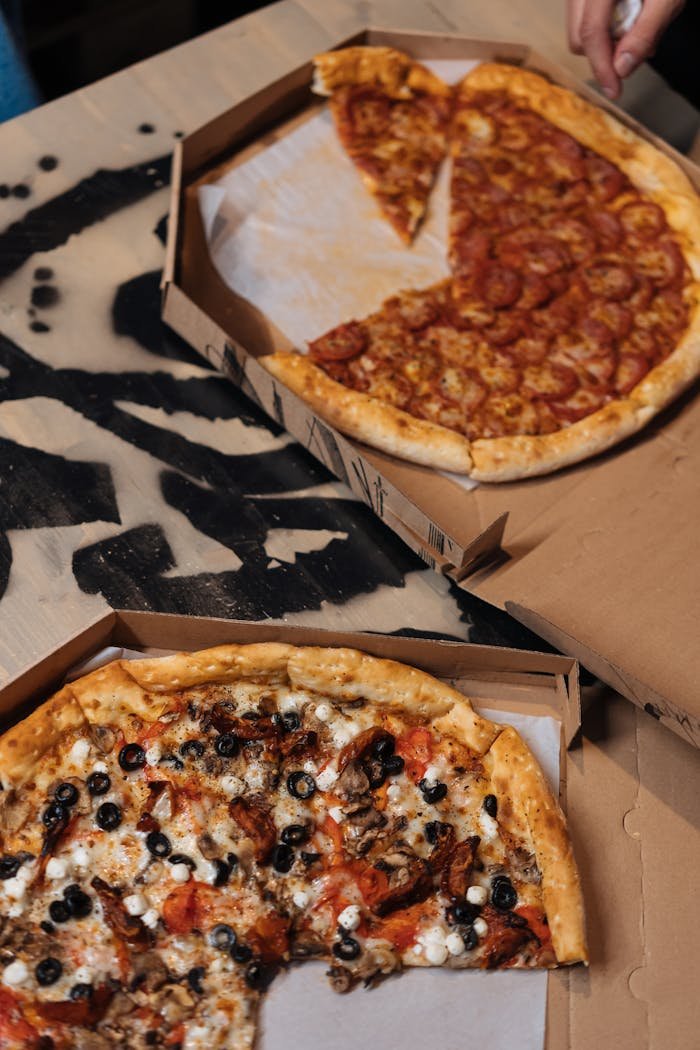 A top view of pepperoni and vegetarian pizzas in boxes on a wooden table, perfect for delivery or fast food themes.